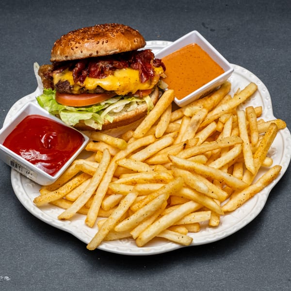 A bacon cheeseburger with lettuce and tomato, served with a side of fries and two dipping sauces.