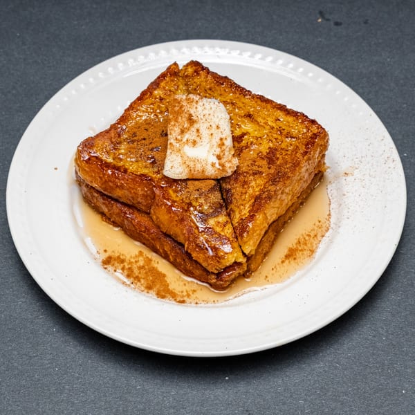 Golden French toast slices with butter, cinnamon, and syrup on a white plate.