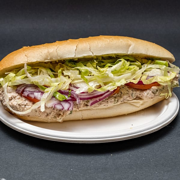 A large tuna sub sandwich with lettuce, red onion, and tomato on a white plate.