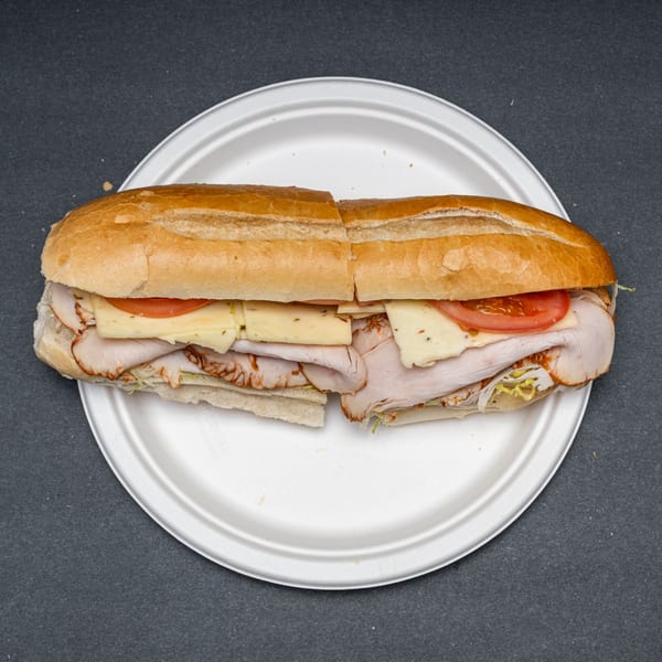 A turkey and cheese sub sandwich, cut in half, on a white paper plate.