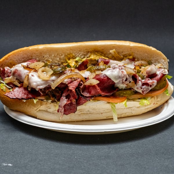 Hearty pastrami sub sandwich with melted cheese, grilled onions, pickles, lettuce, and tomato.
