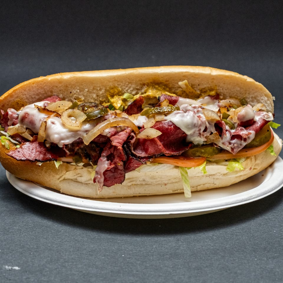 Hearty pastrami sub sandwich with melted cheese, grilled onions, pickles, lettuce, and tomato.