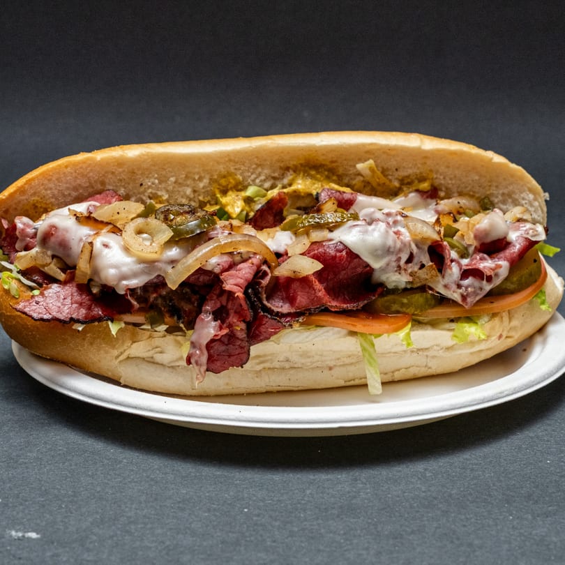 Hearty pastrami sub sandwich with melted cheese, grilled onions, pickles, lettuce, and tomato.