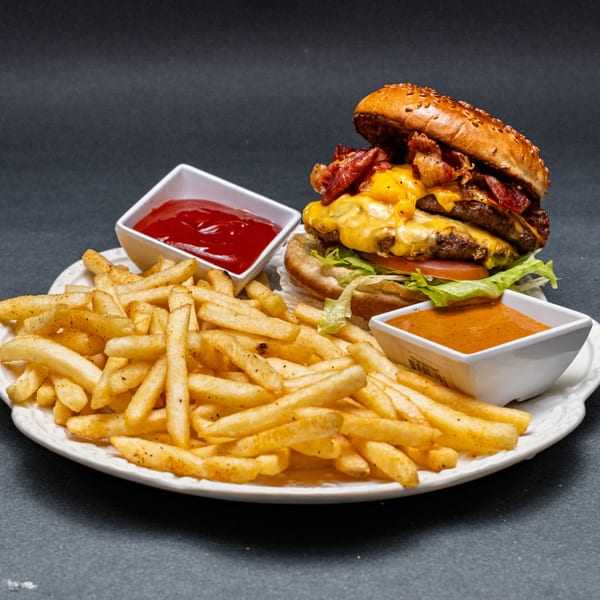 A double bacon cheeseburger with fries, ketchup, and a special sauce on a white plate.