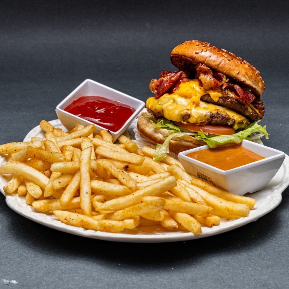 A double bacon cheeseburger with fries, ketchup, and a special sauce on a white plate.