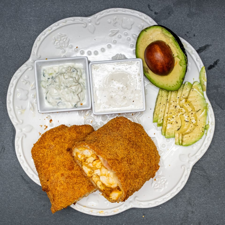 Crispy fried chicken rolls with dipping sauces and sliced avocado on a white plate.
