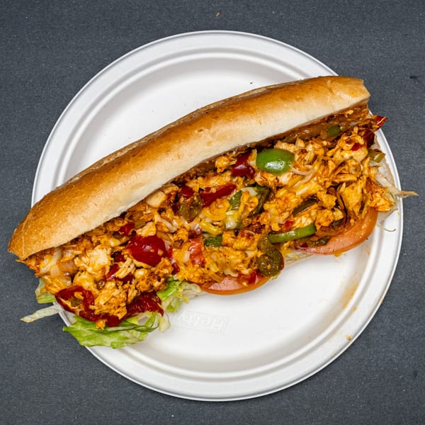A chicken cheesesteak sub with peppers, onions, and lettuce on a white plate.