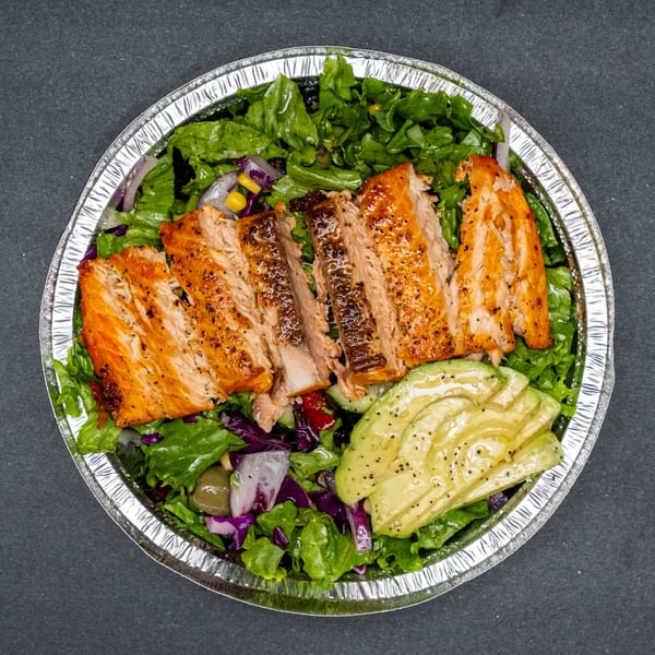 Grilled salmon and avocado slices on a bed of mixed greens in a foil takeout container.