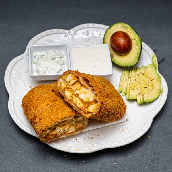 Crispy chicken chimichanga, sliced avocado, and two dipping sauces on a white plate.