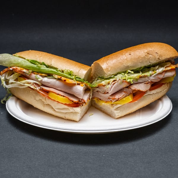 A large sub sandwich, cut in half, filled with meat, cheese, lettuce, and pickles on a white plate.